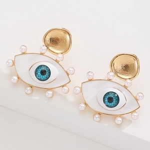 Macro view of gold evil eye earrings with white enamel and pearl accents on white steps