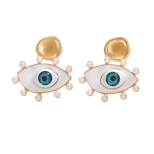 Close-up of golden Evil Eye earrings with blue pupil and white pearl accents on white background