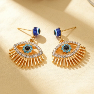Close-up of golden evil eye earrings with blue crystals and intricate diamond settings