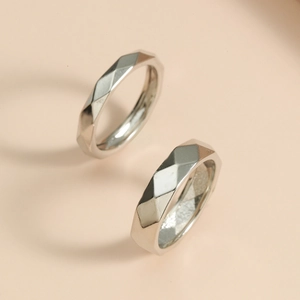 Macro shot of silver minimalist rings with geometric faceted surface on beige background