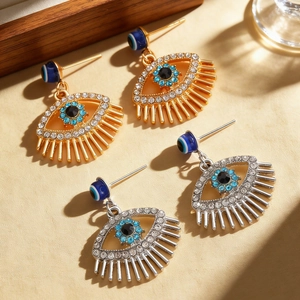 Detail of gold and silver evil eye hoop earrings with blue rhinestones and long lashes