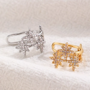 Detailansicht goldener und silberner Stern-Ohrklemmen mit Zirkonia auf Strickhintergrund