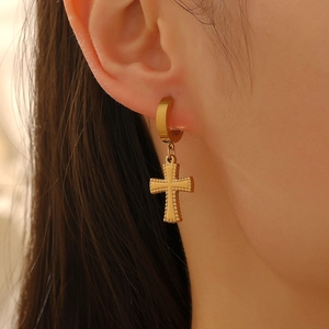 Boucles d'oreilles créoles dorées en acier inoxydable avec croix portées par un mannequin