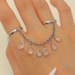 Detailed view of silver linked finger rings with hanging clear teardrop crystal pendants