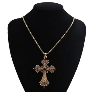 Detail of gothic gold cross necklace with red gemstone on black velvet bust