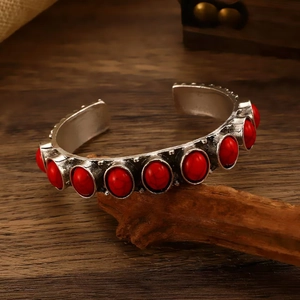 Macro detail of vintage silver-tone bangle featuring red textured stones on wood background