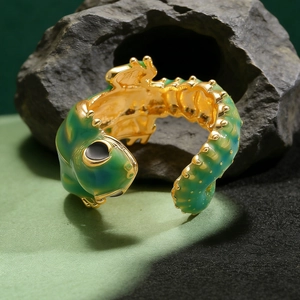 Macro view of green enamel lizard ring with gold accents on a dark stone background