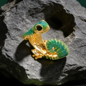 Macro shot of gold-plated lizard ring with green enamel finish on grey textured stone