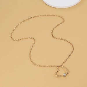 Détail d'un collier chaîne trombone doré avec un grand pendentif cœur ajouré et zircons