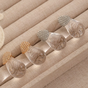 Macro shot of clear teardrop earrings with gold and silver diamond bases on beige tray