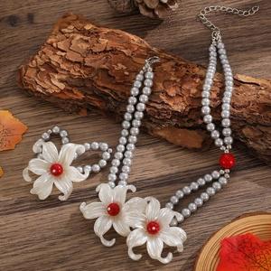 Detailansicht der zweireihigen grauen Perlenkette und des Armbands mit weißen Lilienblüten
