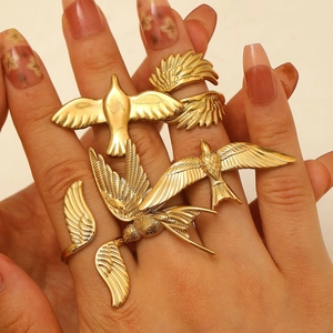 Detailed close-up of golden bird and feather adjustable rings worn on hand model