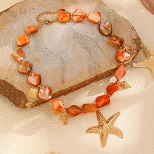 Dettaglio della collana di conchiglie arancioni con ciondoli a stella marina dorata su sabbia
