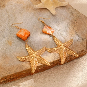 Dettaglio di orecchini lunghi in oro con perle in resina rosa e ciondoli a stella marina