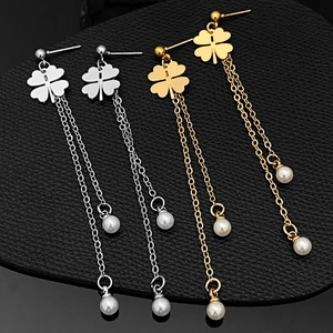 Detalle de pendientes de trébol con borlas largas y perlas en acabado dorado y plata