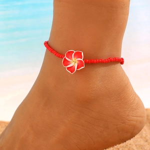 Primer plano de una tobillera de cuentas rojas con colgante de flor de frangipani en la playa