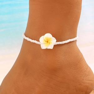 Tobillera bohemia de playa con cuentas blancas y una flor de plumeria amarilla en la arena