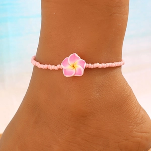 Detalle de tobillera de cuentas rosas con dije de flor de plumeria para la playa