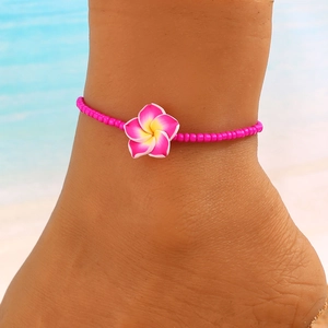 Detalle de tobillera bohemia con cuentas rojo rosa y colgante de flor de plumeria amarilla