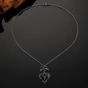 Gothic punk heart necklace with bow and cross pendant on dark reflective surface