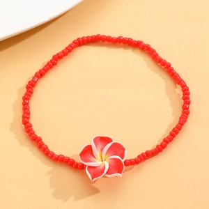 Detalle de tobillera de cuentas rojas con colgante de flor de frangipani en fondo naranja cálido