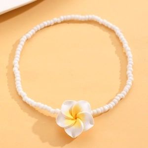 Primer plano de tobillera bohemia de cuentas blancas con flor de plumeria sobre fondo naranja