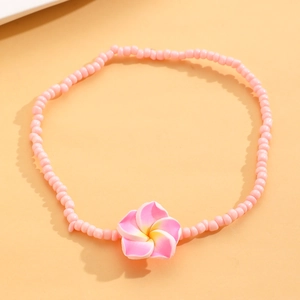 Primer plano de una tobillera de cuentas rosas con un dije detallado de flor de plumeria