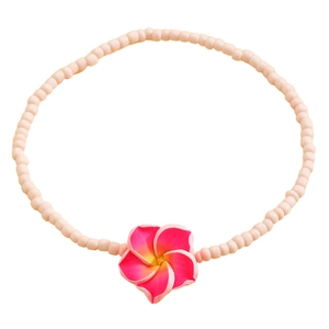 Detalle de tobillera bohemia de cuentas con un colgante de flor de frangipani rosa y amarillo