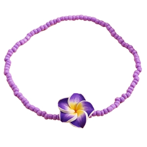 Detalle de tobillera de cuentas moradas con un dije de flor de plumeria amarilla y violeta
