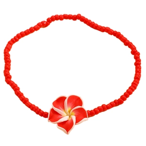 Detalle de tobillera bohemia de cuentas rojas con colgante de flor de plumeria blanca