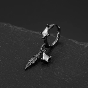 Detail of black feather earring with kite-shaped zircon on textured stone surface