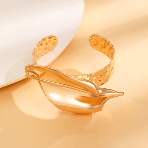 Dettaglio macro del bracciale rigido a fiore in metallo dorato lucido con trama martellata