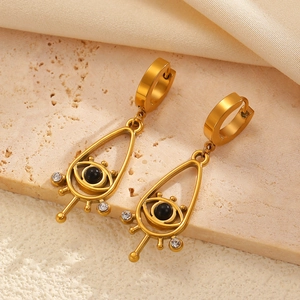 Détail de boucles d'oreilles œil protecteur dorées avec perles noires sur pierre beige