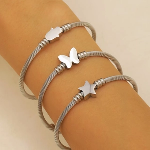Detalle de pulseras de cable plateado con colgantes de Hamsa, mariposa y estrella