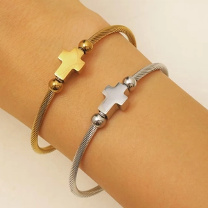 Detalle de pulseras de cable de acero trenzado con dijes de cruz en acabado oro y plata