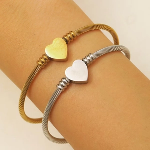 Detalle de brazaletes de cable trenzado con dije de corazón en acabados de oro y plata