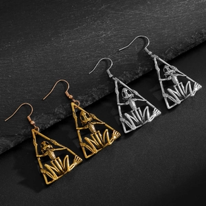 Pendientes de calavera geométrica gótica en oro y plata sobre fondo de piedra oscura