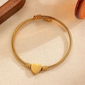 Vista macro detallada del dije de corazón en un brazalete de alambre dorado trenzado