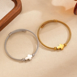 Detalle de pulseras de cable trenzado en oro y plata con un motivo de cruz minimalista