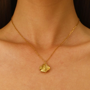 Close-up of a delicate gold fish pendant necklace worn by a model to show elegant detail
