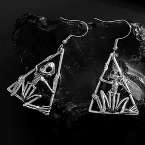 Pendientes de rana calavera gótica en marco triangular sobre fondo de cristal oscuro