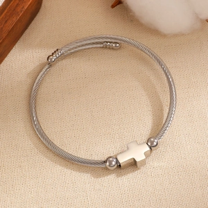 Detalle de pulsera trenzada de acero de titanio plateado con cruz pulida y cuentas bola