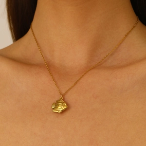 Detailed view of an elegant gold fish pendant necklace worn around the model's neck