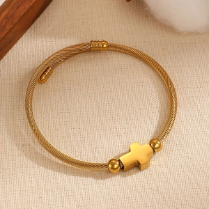 Detalle de pulsera de cable dorado trenzado con cruz pulida y cuentas esféricas