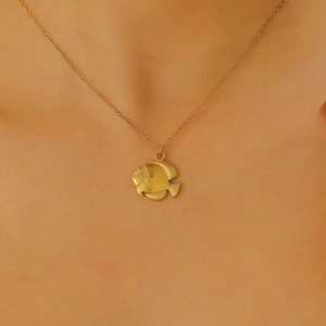 Detailed close-up of a golden tropical fish pendant necklace worn by a model