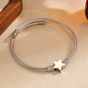Detalle de pulsera rígida de cable plateado con estrella de metal pulido y cuentas