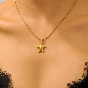 Close-up of a golden sea turtle pendant necklace on a model with snake chain detail