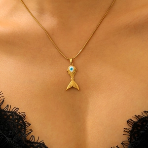 Close-up of golden fish pendant with blue evil eye detail on a delicate snake chain