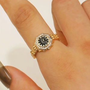 Primo piano di un anello a forma di orologio dorato con quadrante nero e zirconi al dito