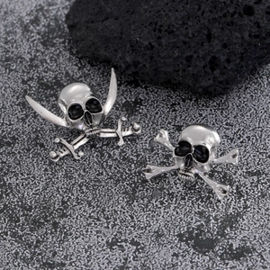Detail of vintage silver pirate skull and crossbones stud earrings on dark volcanic rock